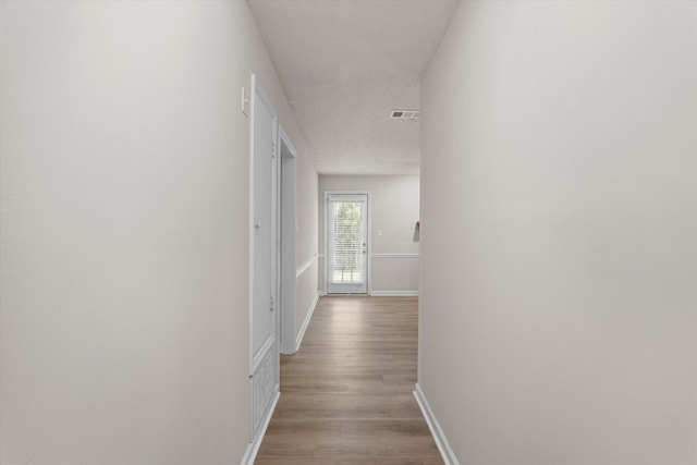 hallway featuring visible vents, baseboards, and wood finished floors