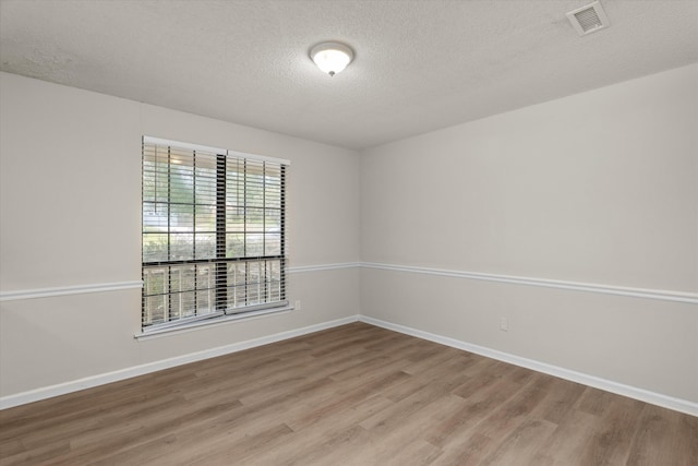 spare room featuring light wood-style flooring, a textured ceiling, baseboards, and visible vents
