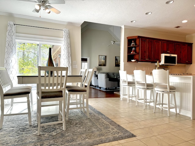 dining room with ceiling fan, light tile patterned floors, a textured ceiling, and ornamental molding