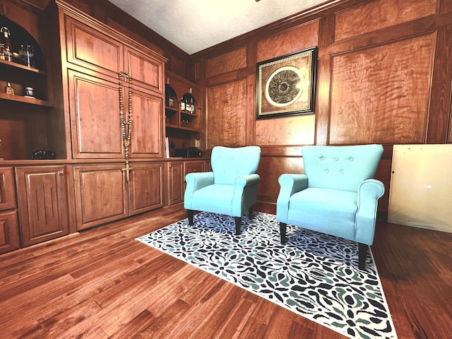 sitting room with built in shelves, wood walls, hardwood / wood-style floors, and a textured ceiling