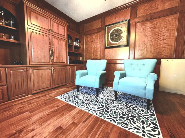 sitting room with built in shelves, wood walls, hardwood / wood-style floors, and a textured ceiling