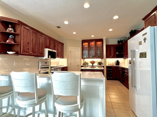 kitchen with appliances with stainless steel finishes, a breakfast bar, a textured ceiling, crown molding, and light tile patterned floors