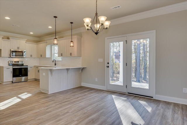 kitchen with appliances with stainless steel finishes, a kitchen breakfast bar, pendant lighting, light hardwood / wood-style floors, and white cabinets