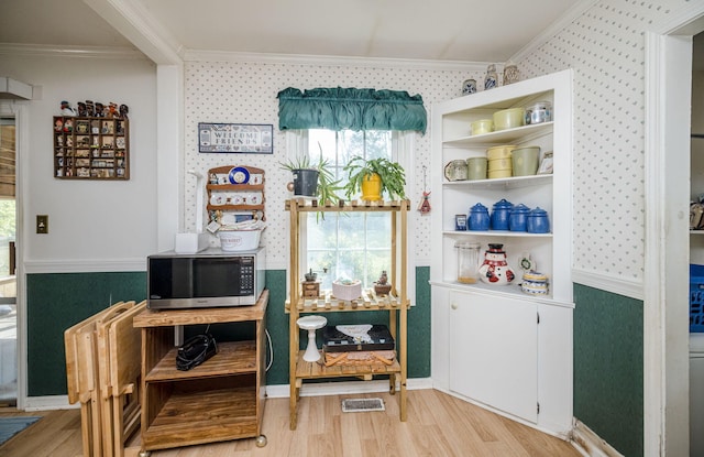 bar with crown molding, stainless steel microwave, wallpapered walls, and light wood-type flooring