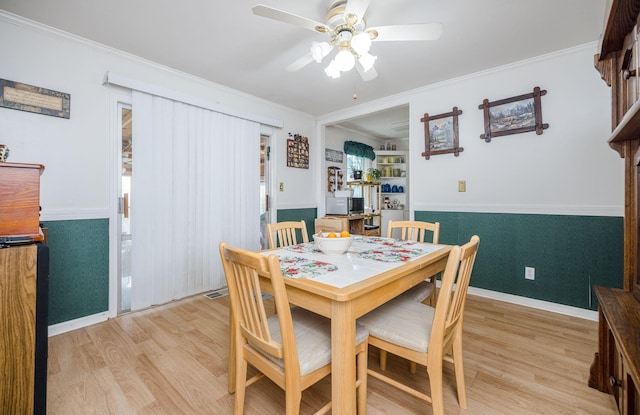 dining space featuring light wood-style floors, a wainscoted wall, ceiling fan, and crown molding