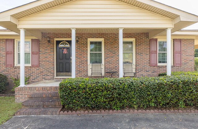 view of exterior entry with a porch and brick siding