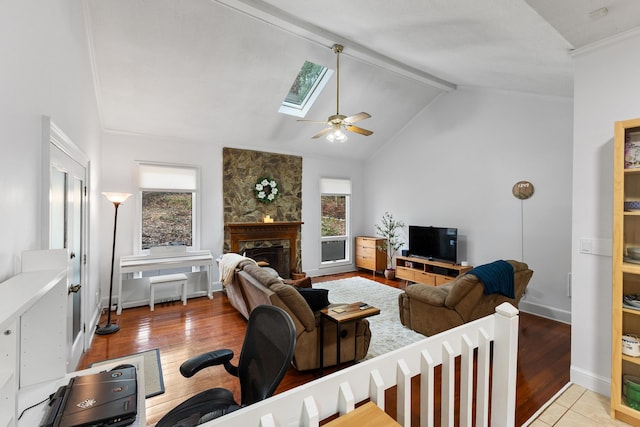 living room with a stone fireplace, ceiling fan, vaulted ceiling with skylight, and light hardwood / wood-style flooring