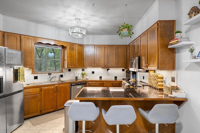 kitchen featuring a breakfast bar, sink, appliances with stainless steel finishes, light tile patterned flooring, and kitchen peninsula