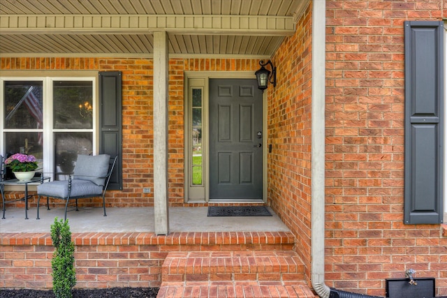 entrance to property featuring a porch and brick siding