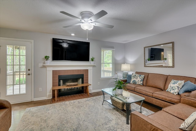 living room featuring wood finished floors, a wealth of natural light, a tile fireplace, and ceiling fan