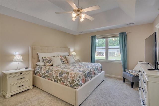 bedroom featuring visible vents, light carpet, ceiling fan, and a tray ceiling