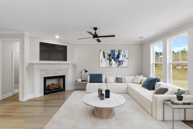 living room featuring crown molding, light wood-type flooring, ceiling fan, and a fireplace