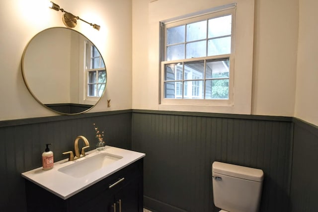 half bathroom with a wainscoted wall, toilet, and vanity