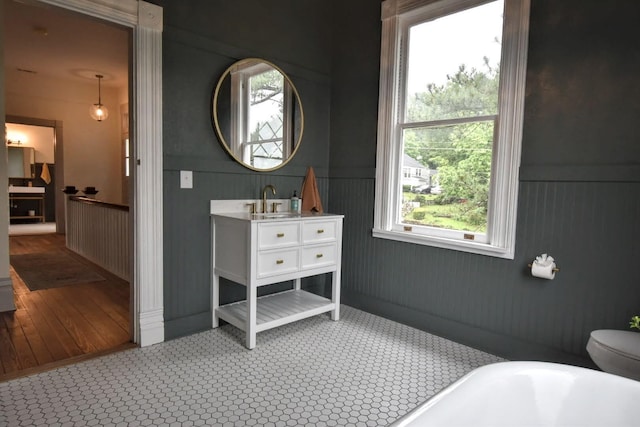 full bath featuring wainscoting, a soaking tub, a healthy amount of sunlight, and vanity