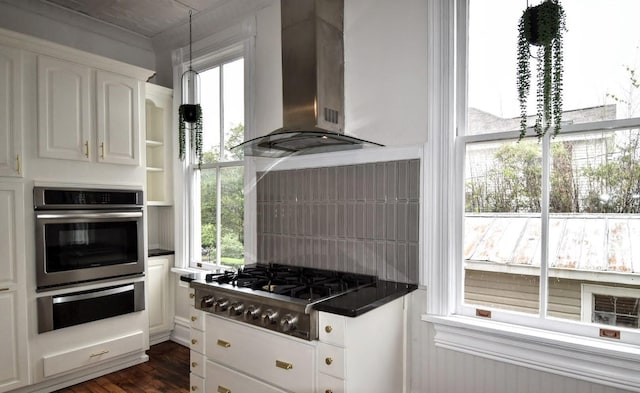 kitchen with a warming drawer, stainless steel appliances, white cabinetry, dark countertops, and wall chimney range hood