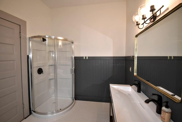 full bathroom featuring a notable chandelier, a wainscoted wall, a stall shower, and vanity