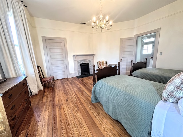 bedroom featuring a notable chandelier, a fireplace with flush hearth, visible vents, and wood finished floors