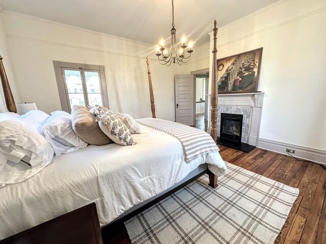 bedroom with an inviting chandelier, hardwood / wood-style flooring, a fireplace, and crown molding