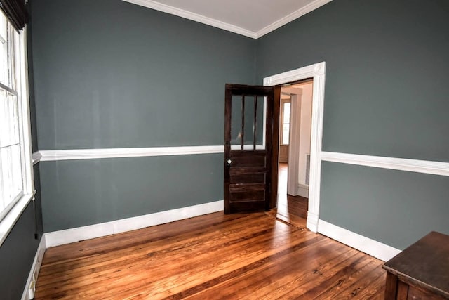 empty room with crown molding, wood finished floors, and baseboards