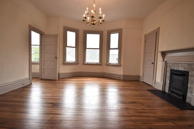 unfurnished living room featuring a chandelier, a tile fireplace, dark wood-type flooring, and baseboards