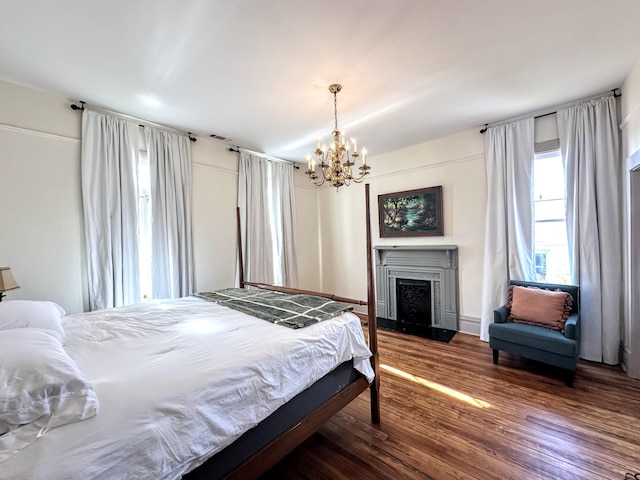 bedroom featuring a chandelier, visible vents, a fireplace with raised hearth, and wood finished floors