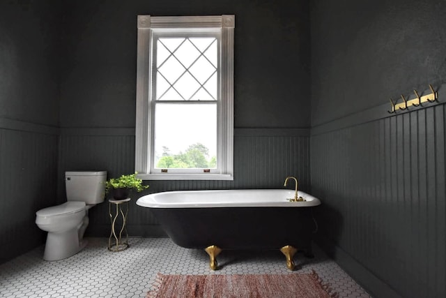 full bathroom featuring tile patterned floors, a wainscoted wall, a freestanding bath, and toilet