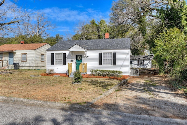 view of front facade featuring roof with shingles, a chimney, and a front yard