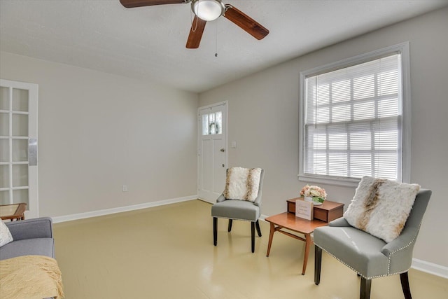 living area with a ceiling fan and baseboards