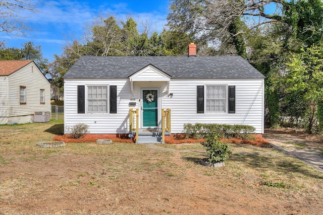 bungalow-style home with cooling unit, roof with shingles, a chimney, and a front lawn