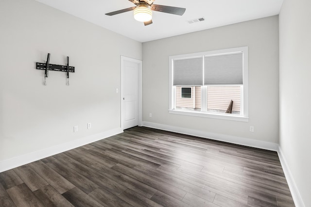 empty room with baseboards, visible vents, a ceiling fan, and dark wood-type flooring