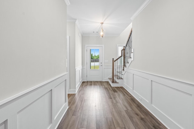 doorway featuring a chandelier, ornamental molding, dark wood-style flooring, and a decorative wall