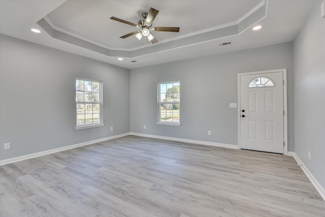 interior space with a tray ceiling, visible vents, light wood-style floors, a ceiling fan, and baseboards