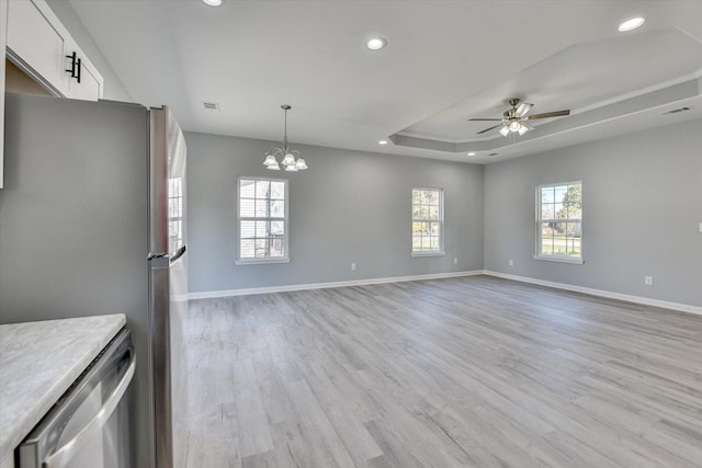 kitchen with appliances with stainless steel finishes, open floor plan, a tray ceiling, light countertops, and white cabinetry