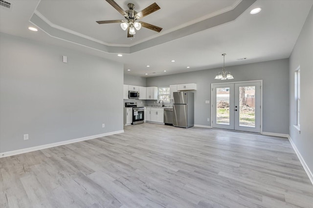 unfurnished living room with a tray ceiling, light wood-type flooring, a sink, and baseboards