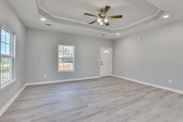 empty room with baseboards, light wood-style floors, a raised ceiling, and a healthy amount of sunlight