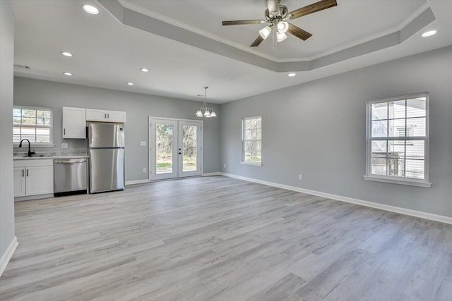 unfurnished living room featuring light wood finished floors, a tray ceiling, a sink, and baseboards