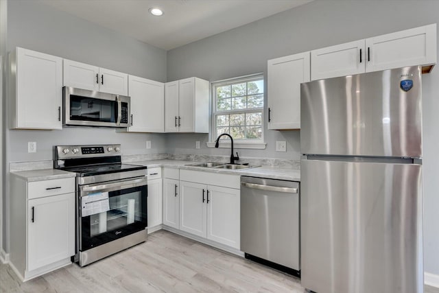 kitchen with white cabinets, stainless steel appliances, a sink, and light countertops