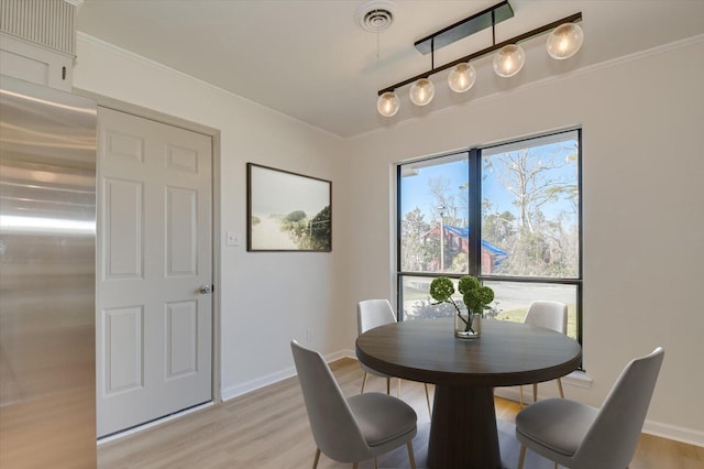 dining area featuring light wood-type flooring, visible vents, baseboards, and ornamental molding