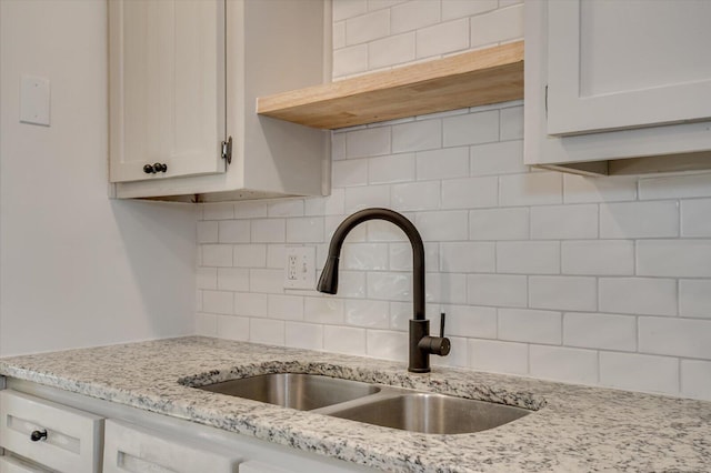 kitchen featuring a sink, light stone countertops, tasteful backsplash, and white cabinetry