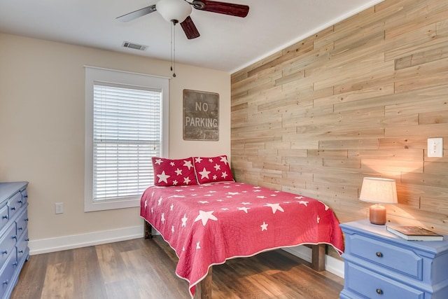 bedroom featuring visible vents, wood walls, wood finished floors, baseboards, and ceiling fan
