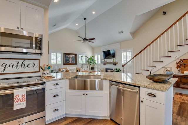 kitchen with visible vents, open floor plan, a large fireplace, a sink, and stainless steel appliances