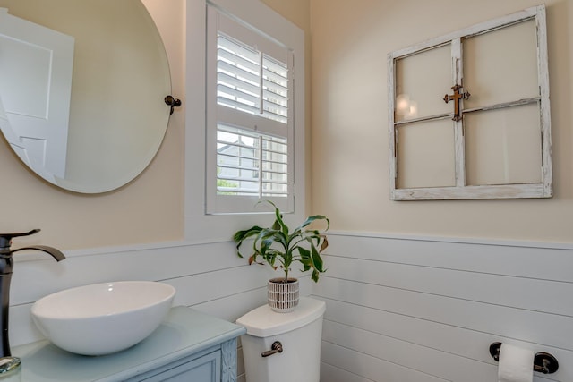 half bathroom with vanity, wainscoting, and toilet