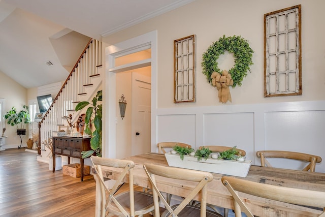 dining area featuring wainscoting, wood finished floors, stairway, and a decorative wall