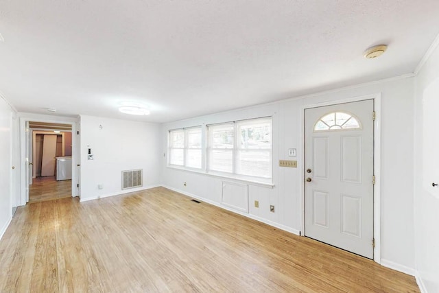 entrance foyer with ornamental molding, washer / dryer, a healthy amount of sunlight, and light hardwood / wood-style floors