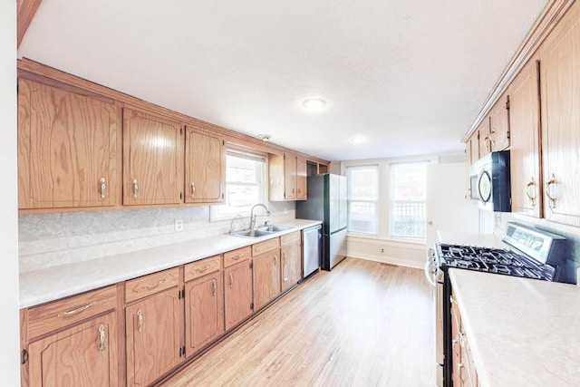 kitchen with stainless steel appliances, sink, backsplash, and light wood-type flooring