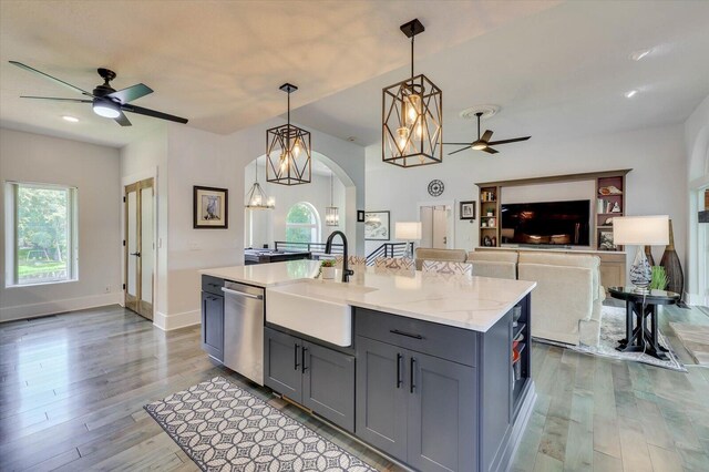 kitchen with sink, stainless steel dishwasher, light stone countertops, an island with sink, and decorative light fixtures