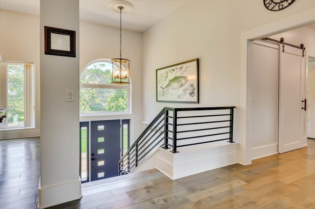 foyer entrance with hardwood / wood-style floors, a barn door, a towering ceiling, and a chandelier