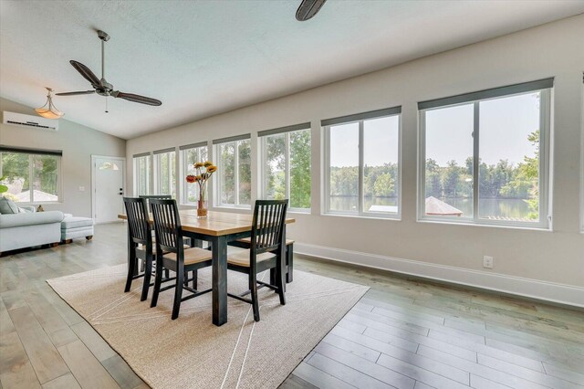 dining area featuring a wall mounted AC, light hardwood / wood-style floors, vaulted ceiling, and ceiling fan