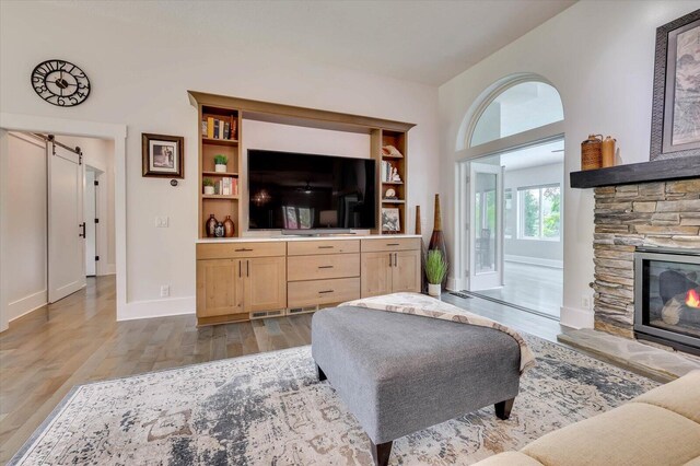 living room with hardwood / wood-style floors, a barn door, built in features, and a stone fireplace