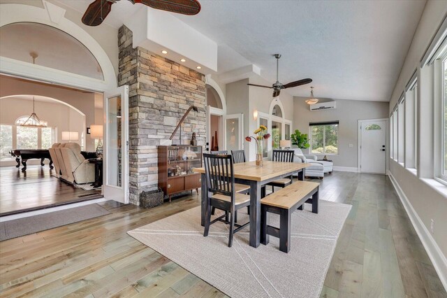 dining room with hardwood / wood-style flooring, a healthy amount of sunlight, high vaulted ceiling, and a wall mounted AC